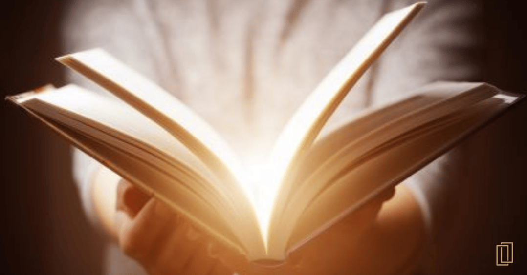 Hands holding an open book with a warm light radiating out of the book spine